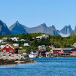 Red rorbuer cabins on stilts over a Lofoten harbor with mountains behind
